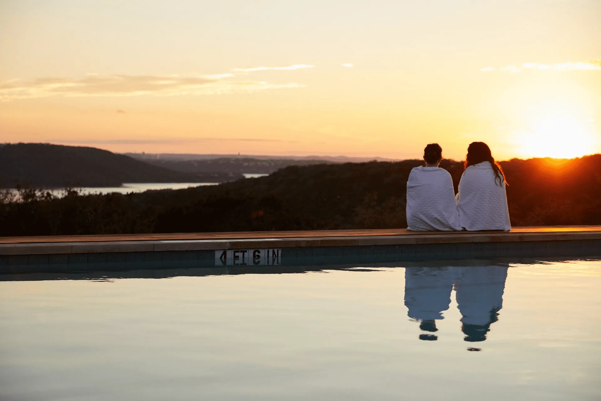 two people sitting by the pool watching the sun set