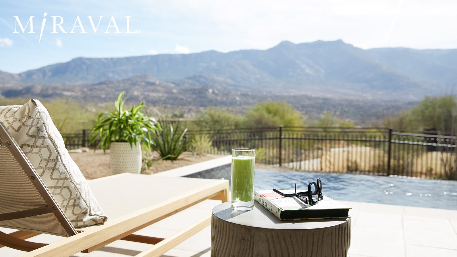 Lounge chair on pool deck overlooking landscape with a green smoothie, book and glasses on side table