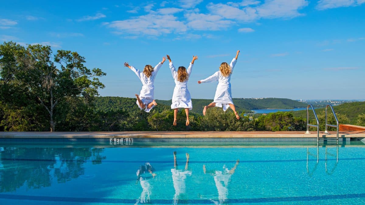 three people jumping into the air beside a pool