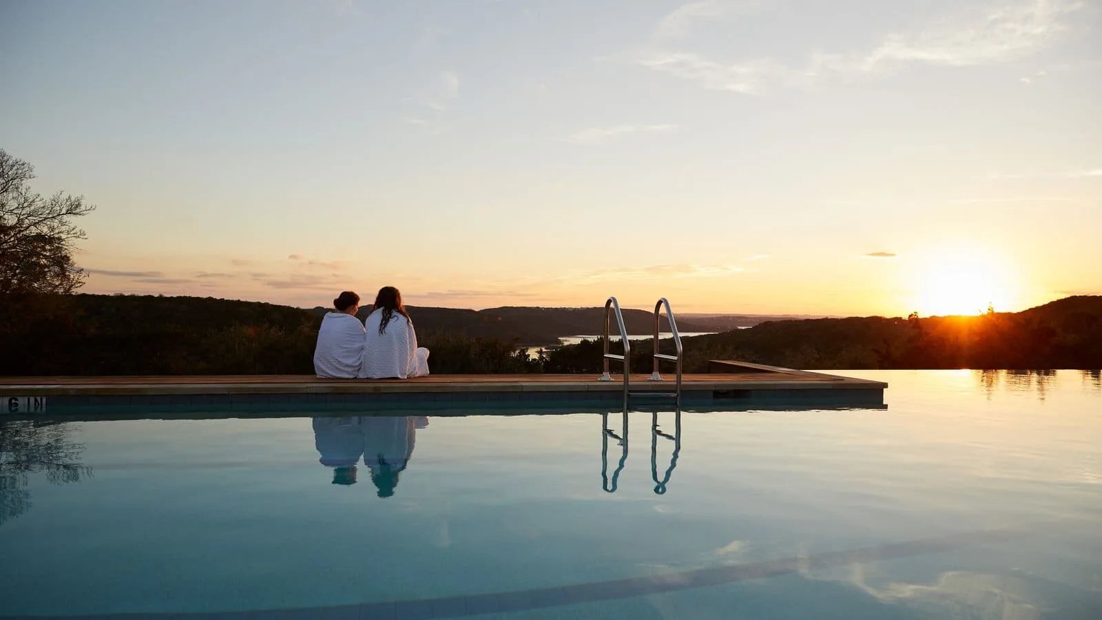 two people in robes watching the sun set by the pool