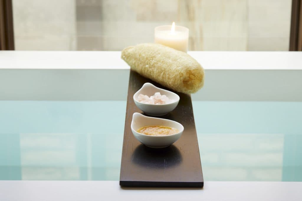 Bath oil and salt, sponge and candle on bath tray over bath