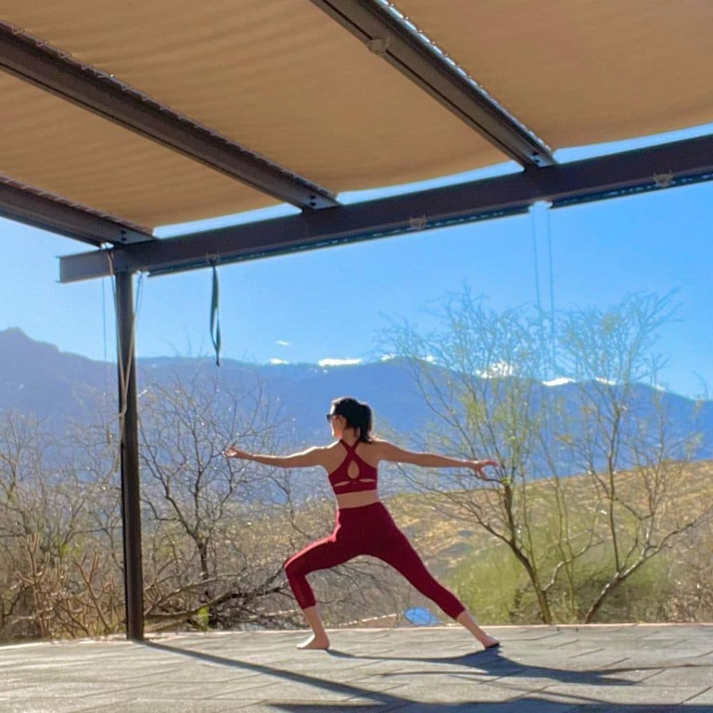 Lydia Fenet in exercise outfit doing yoga outside on sun covered patio looking at mountain landscap