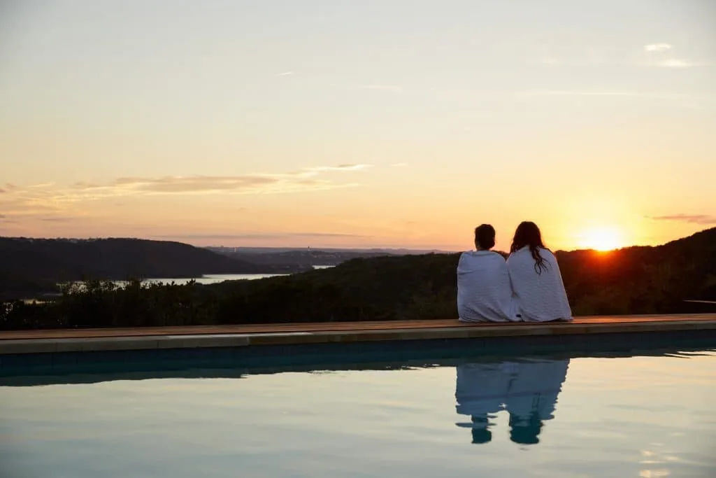 two people in robes sitting by the pool watching the sunset