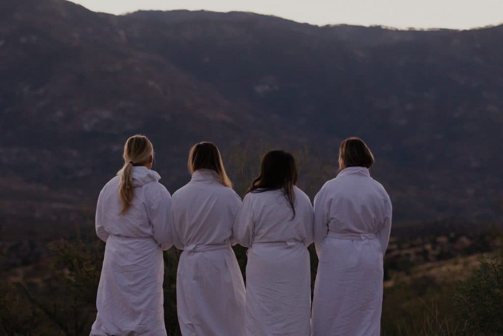 Four women in robes looking at mountains during sunset